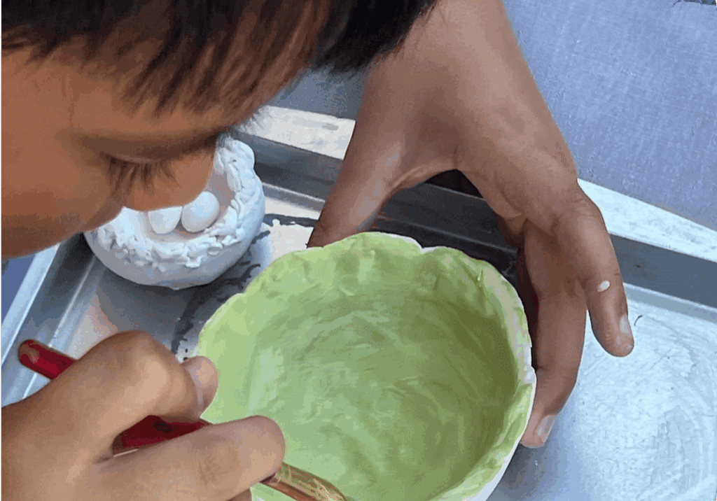 Child painting a green ceramic bowl.